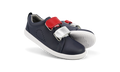 The Bobux Kids Plus KP SWITCH Grass Court Navy 837712 are navy leather sneakers with white soles, red and silver removable straps, and perforated side detailing, shown against a plain white background.