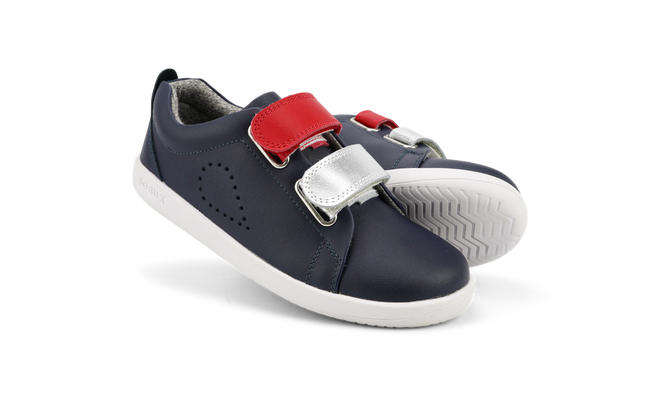The Bobux Kids Plus KP SWITCH Grass Court Navy 837712 are navy leather sneakers with white soles, red and silver removable straps, and perforated side detailing, shown against a plain white background.