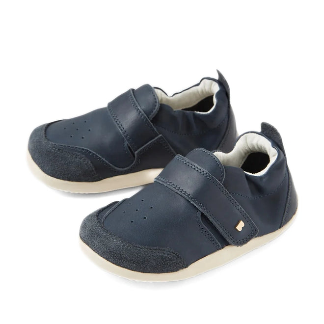 A pair of Bobux XP Explorer Ripple First Walker shoes in navy, featuring beige soles, Velcro straps, and soft suede toe caps. These flexible-soled toddler shoes are perfect for first walkers and are displayed on a white background.