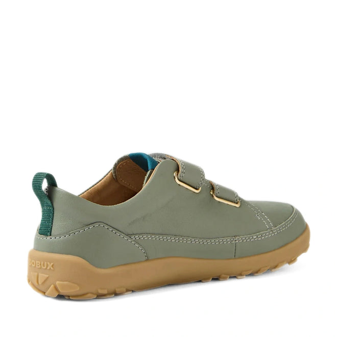 A Bobux KP Kids Plus Dawn Leather Sneaker in Vetiver Green, featuring a tan rubber sole, Velcro straps, a wide toe box, and a teal pull tab at the heel, shown from the back left side.