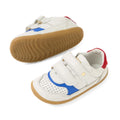A pair of Bobux SU Step Up Hunter Leather Toddlers Sneakers in White Salsa, featuring white leather uppers, tan rubber soles, blue and red accents, and two velcro straps on each shoe. One shoe is upright while the other displays the sole—perfect first walker shoes for your toddler.