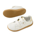 The Bobux Kid+ Plus KP Maverick Leather Sneaker in White Gold features two adjustable velcro straps, stylish gold heel accents, and tan rubber soles. These comfortable leather children’s sneakers are designed for everyday adventures. One shoe is displayed from the side view and the other from the sole.