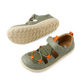 A pair of Bobux Kid+ KP Rocky Leather Closed Toe Sandal Vetiver Green Barefoot for kids features green and orange leather with white soles. One sandal stands upright, displaying the top and side view, while the other is flipped over to reveal the tread pattern on the sole. Designed as zero drop barefoot shoes, these closed-toe sandals combine style and comfort for little feet.
