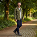A man in a tree lined path wearing navy trousers a green jacket and grey shirt waering The Barbour Mens Harefield Derby Lace Up Shoe in slate grey suede features brown rubber soles and is displayed on a white background.