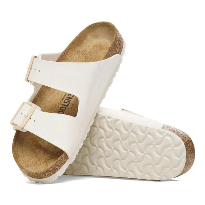 A pair of Birkenstock Arizona slides in a soft eggshell White sandals with brown soles on a white background. Showing the top ogf one foot and the outer sole of the other.