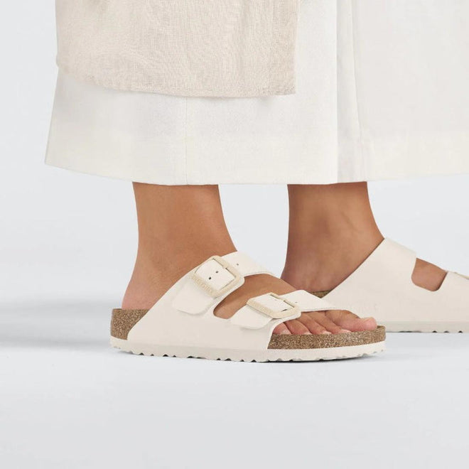 Beige Eggshell Birkenstock Arizona Double Strap  sandals worn with white pants on a light gray background.,
4066648369509,
4066648369547,
4066648369585,