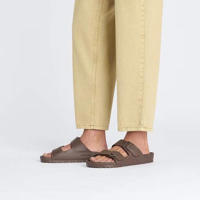 A person is shown from the legs down wearing light yellow pants and BIRKENSTOCK Arizona EVA Brown Roast sandals (REGULAR width) against a plain light background., 4066648335047, 4066648335085, 4066648338321, 4066648338369, 4066648338406, 50615