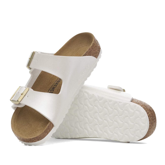 A pair of Birkenstock Kids Arizona Metallic Pearl White Narrow Slides with two adjustable buckled straps and a supportive cork footbed. One slide stands upright while the other lies flat, showing the textured white sole.