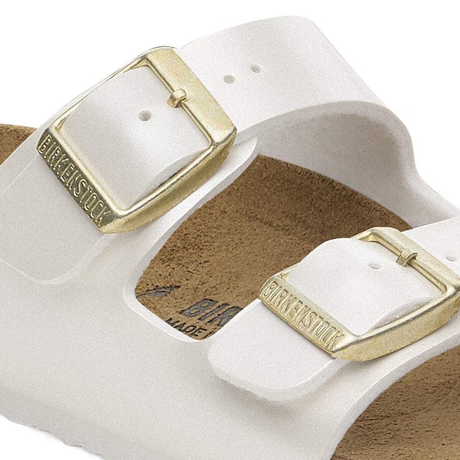 Close-up of Birkenstock Kids Arizona Metallic Pearl White Narrow Slides featuring two gold buckles engraved with the logo and an adjustable cork footbed in the background., 48068, 48069, 48070, 48071, 48072, 48073, 48074, 48075, 48076