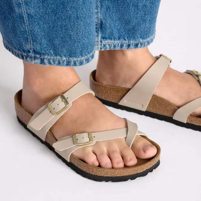 A picture of a womens feet wearing blue denium jeans and Mayari Birkenstock toe loop sandals in sandcastle beige looking top down., 4067707169030,
4067707169078,
4067707169115,
4067707169153,