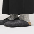 Close-up of a person wearing Birkenstock Amsterdam Felt Wool Clog in Anthracite Grey (Regular Width) with thick light gray ribbed socks and black pants, showcasing the supportive cork footbed and stylish, comfortable design., 52004, 52005, 4067707295241, 4067707295289, 4067707295326, 4067707295364, 4067707295401, 4067707295449, 4067707295487, 52013, 52014
