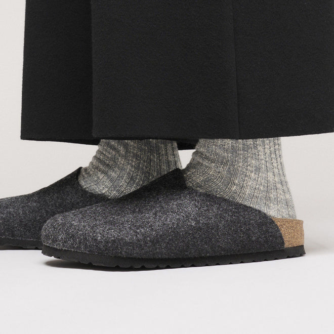 Close-up of a person wearing Birkenstock Amsterdam Felt Wool Clog in Anthracite Grey (Regular Width) with thick light gray ribbed socks and black pants, showcasing the supportive cork footbed and stylish, comfortable design., 52004, 52005, 4067707295241, 4067707295289, 4067707295326, 4067707295364, 4067707295401, 4067707295449, 4067707295487, 52013, 52014