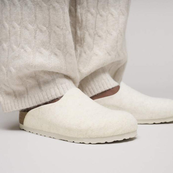 A person in textured cream pants and matching Birkenstock Amsterdam Felt Wool Clog Eggshell Off White (Regular Width) with cork-latex footbed, standing on a light surface., 51708, 51709, 4067707298440, 4067707298488, 4067707298525, 4067707298563, 51714, 51715, 51716, 51717, 51718