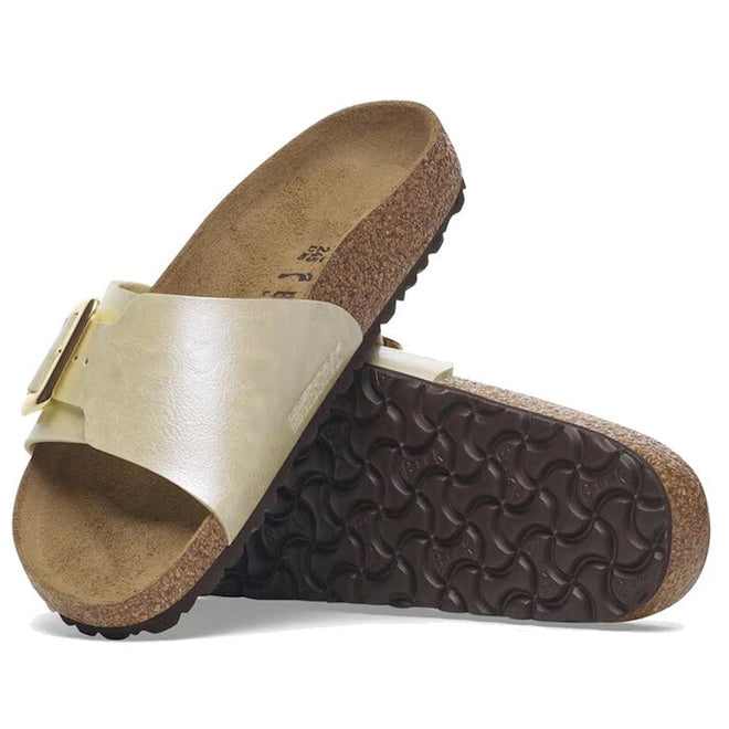 A pair of Birkenstock Womens Catalina Cushion Buckle Birko Flor sandals in pearl white (regular width) with shiny straps, large buckles, cork-latex footbeds, and dark brown textured soles—one sandal stands upright, the other rests on its side.