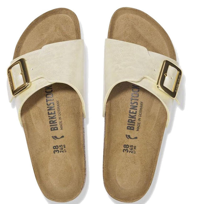 A pair of Birkenstock Womens Catalina Cushion Buckle Birko Flor sandals in pearl white with large gold buckles, supportive cork-latex footbeds, brown soles, sizing details, and "Made in Germany" labels is viewed from above., 4066648995265, 4066648995302, 4066648995340, 4066648995388, 4066648995425, 4066648995463, 47502