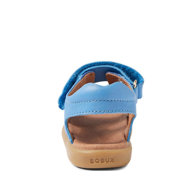 The Bobux IW Iwalk Strand Sandal in Azure Blue features a tan sole, open heel and toe, "BOBUX" on the back, and adjustable ankle straps for a secure fit—shown here from the rear view., 9420068556997, 9420068557000, 9420068557017, 9420068557024, 9420068557031