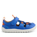 The Bobux IW Iwalk Rocky Dazzling Blue Closed Toe Sandal Barefoot is a kids’ sandal in blue and orange, with a barefoot-shaped toe box, white rugged sole, adjustable Velcro strap, and breathable cutout sides, shown from the side.