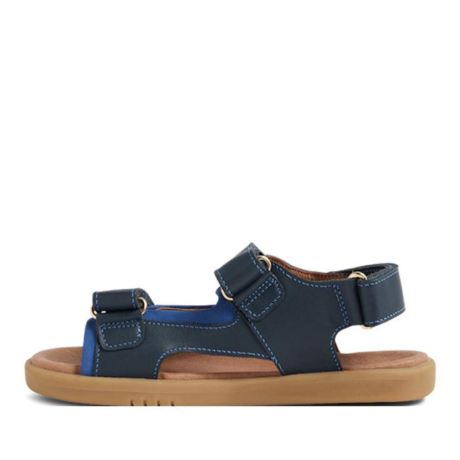 The Bobux Kid+ Plus Strand Navy Open Toe Sandal features adjustable straps, white stitching, a tan cushioned sole, and a breathable design for comfort—perfect for kids' casual wear., 9420068557048, 9420068557055, 9420068557062, 9420068557079, 9420068557086, 9420068557093, 9420068557109