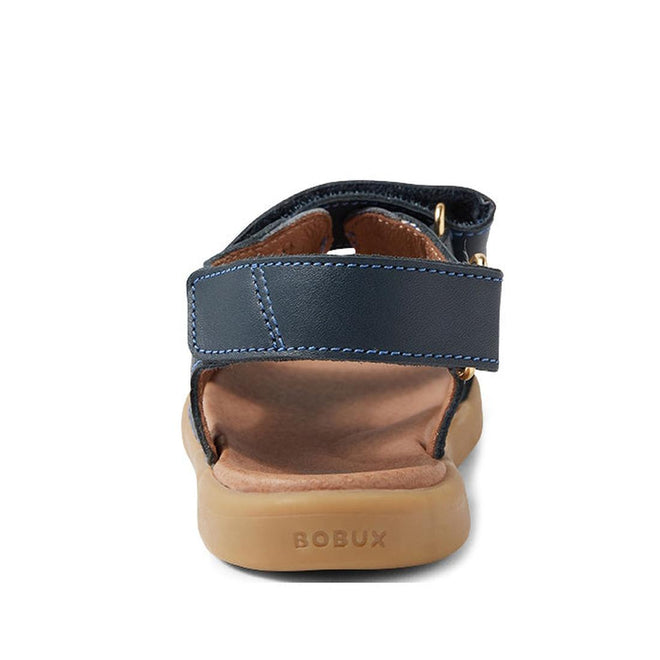 A close-up rear view of the Bobux Kid+ Plus Strand Navy Open Toe Sandal, featuring a navy blue design, brown cushioned sole with BOBUX embossed on the heel, and adjustable Velcro straps for a secure, customizable fit., 9420068557048, 9420068557055, 9420068557062, 9420068557079, 9420068557086, 9420068557093, 9420068557109