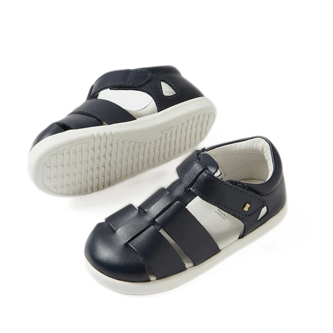 A pair of Bobux IWalk Tidal Closed Toe Quick Dry Sandals in navy (model 634404A) for kids, featuring a unisex design with white soles, crafted from quick-dry leather and equipped with adjustable Velcro straps, displayed on a white background.