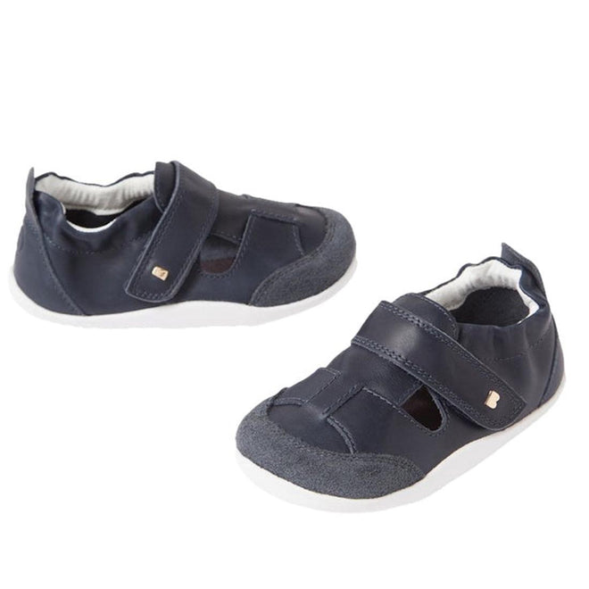 The Bobux XP Explorer Beau First Walker Sandal Navy features velcro straps, white flexible soles, and suede toe caps, displayed on a white background.