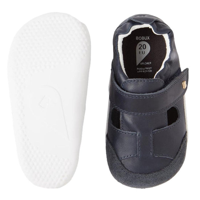 The Bobux XP Explorer Beau First Walker Sandal in Navy features a top view of a navy blue leather sandal with a Velcro strap and a side view displaying its flexible sole, ideal for toddlers taking their first steps., 9420068568808, 9420068568815, 9420068568822, 9420068568839