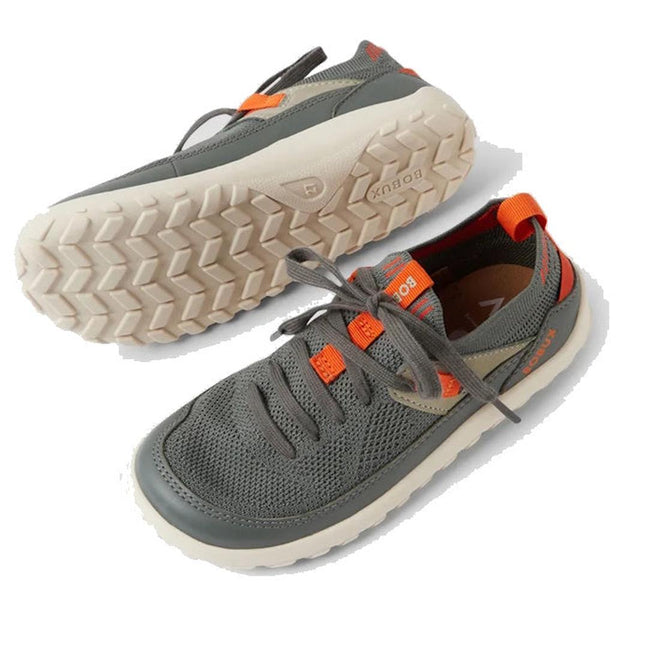 The Bobux Kid+ Meta Knit Barefoot Sneaker in Vetiver Green for juniors features a breathable knit upper, white textured sole, orange accents, and gray laces. One shoe lies on its side to display the sole; the other stands upright., 9420074836014, 9420074836021, 9420074836038, 9420074836045, 9420074836052, 9420074836069, 46358