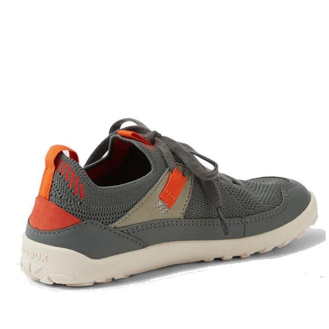 The Bobux Kid+ Meta Knit Barefoot Sneaker in Vetiver Green for juniors has orange and tan accents, a breathable knit upper, mesh detailing, a white textured sole, visible laces, and a heel pull tab. Shown angled on a white background., 9420074836014, 9420074836021, 9420074836038, 9420074836045, 9420074836052, 9420074836069, 46358