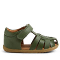 The Bobux Step Up Todders Sandal Harbor Closed Toe Bronze Green is a children's green leather sandal with a woven design, velcro strap, and flexible light brown sole—perfect for first walkers. Side view shown on white background.