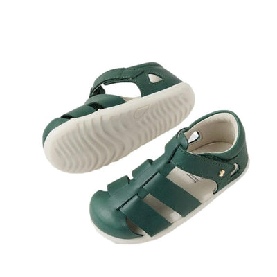A pair of Bobux Step Up US Tidal Rainforest Green Closed Toe Sandals for toddlers, made from quick-drying leather with white rubber soles, are displayed on a white background—one upright, the other showing its sole.