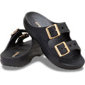 The Crocs Womens Classic Metallic Buckle Saturday Sandal Slide in black features two adjustable straps with shiny gold buckles, a textured footbed for Crocs Comfort, and the signature logo.
