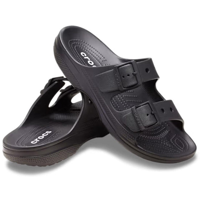 The Crocs Womens Classic Saturday Sandal Slide Black features two adjustable buckle straps; one sandal upright and the other flat, highlighting Crocs comfort with a textured footbed and sole.