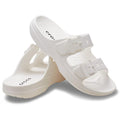 The Crocs Womens Classic Saturday Sandal Slide in white features two adjustable buckle straps on each shoe for a personalized fit—one sandal stands upright, while the other leans against it.