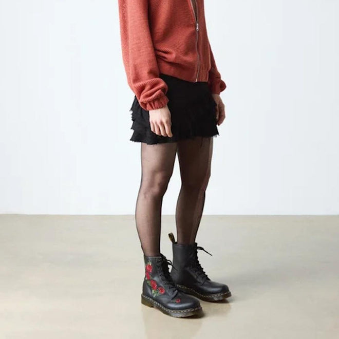 Person wearing a rust zip-up jacket, black mini skirt, sheer black tights, and Dr Martens 1460 Vonda Red Roses Softy T Leather Boots, standing indoors on a light floor against a plain background., 190665206036, 190665206043, 190665206050, 190665206074, 190665206081, 190665206098