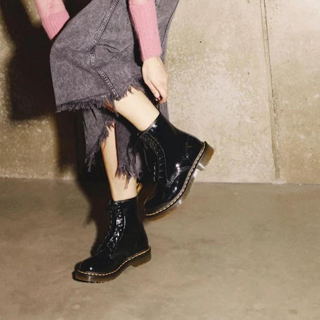 Person wearing DR Martens 1460 black patent leather boots with a textured beige background.,
883985035249,
883985035256,
883985035270,