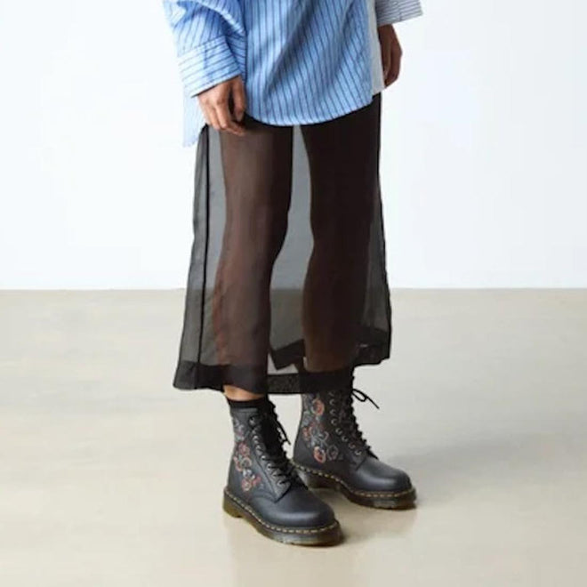 A person in a blue striped shirt, black sheer skirt over black pants, and black Dr Martens 1460 Vonda TF Tavern Floral Genix Nappa Leather boots stands on a light-colored floor., 47991, 190665742619, 190665742626, 190665742633, 190665742657, 47996, 47997