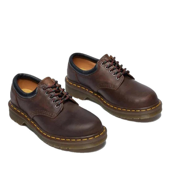 The Dr Martens 8053 Crazy Horse Dark Brown Leather 5 Eye shoe is a unisex lace-up with black trim, visible stitching, and thick air-cushioned rubber soles featuring yellow stitching around the edges., 52072, 52073, 800090801651, 800090801675, 800090801682, 800090801699, 800090801712