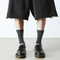 Person wearing black shorts, Dr Martens Socks Double Doc Sock Unisex Charcoal Organic, and black lace-up shoes stands on a light-colored floor against a plain white background., 190665563108, 190665563092