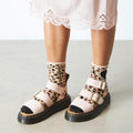 A model styling Dr Martens Gryphon quad sandals with leopard print socks with pink sandals on a light background,
190665714630,
190665714647,
190665714661,
