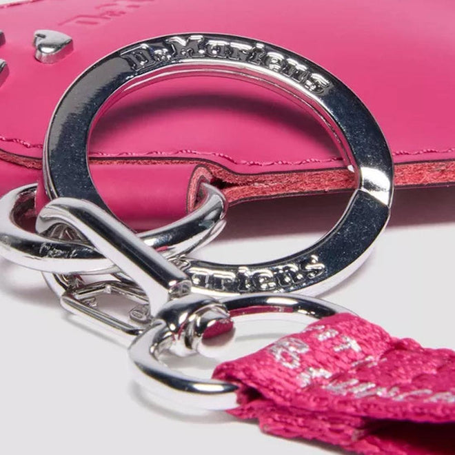Close-up of silver keychain Dr Martens Heart Charm with pink tassel against a pink background.,
190665739800,