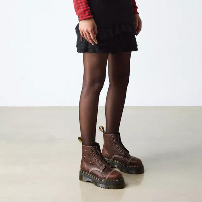 A person wears a black skirt, black sheer tights, and Dr Martens Sinclair Flower Dark Brown Grizzly Leather Boots with a platform Quad sole, standing on a light floor against a plain white background., 51903, 51904, 190665777116, 190665777123, 190665777147, 51909, 51910