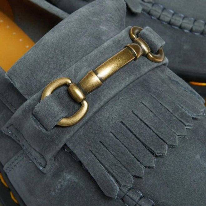 Close-up of the Dr. Martens Adrian Snaffle Loafer in washed denim tumbled nubuck, featuring fringe details, visible stitching, and a decorative metal horsebit accent across the front.