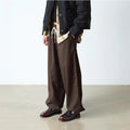A person stands indoors with hands in pockets, wearing loose brown pinstriped pants, a beige shirt, a black jacket, and Dr Martens Temara Cherry Red Arcadia Leather Loafers. Their face is not visible., 190665747560, 190665747577, 190665747591, 52060, 52061