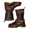 The Dr Martens Anistone Hi Flower Bex Grizzly Dark Brown boots feature yellow stitching, floral embossing, buckles, metal plaques, rugged soles, and back pull tabs for a biker-inspired look.