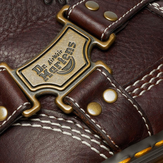 Close-up of the Dr Martens Anistone Hi Flower Bex Grizzly Dark Brown showing detailed white stitching, brass rivets, and a metal Dr. Martens logo plate on the brown leather strap.