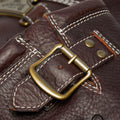Close-up of the Dr Martens Anistone Hi Flower Bex Grizzly Dark Brown bag, showing textured brown leather, white stitching, a brass buckle, and metal rivets. Stitching and hardware details are clearly visible.