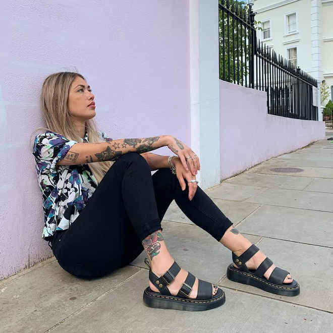 Woman sitting on a sidewalk wearing  Dr Martens Black Gyphon black sandals in pisa leather and a colorful shirt against a light purple wall.,
190665318654,
190665318661,
190665318678,
190665318685,
190665318692,
190665318708,
190665318715,