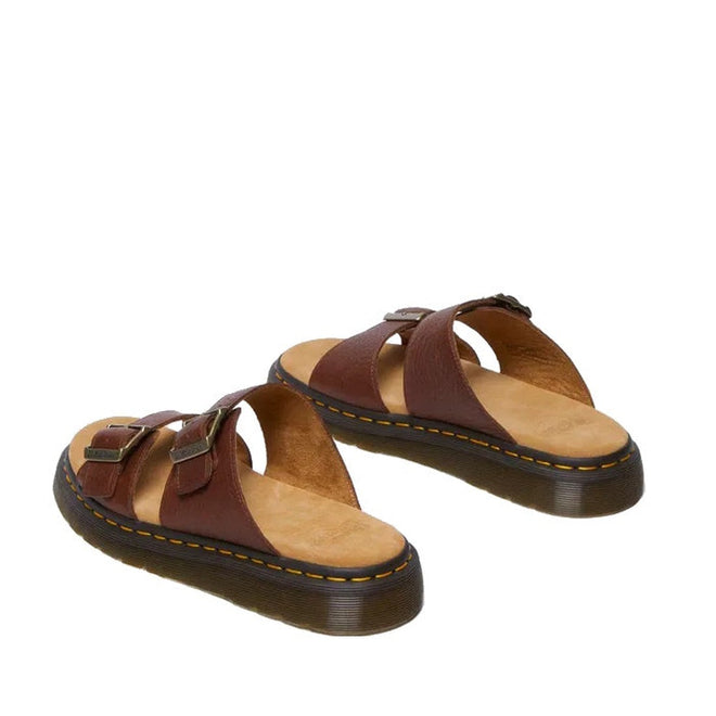 A pair of Dr Martens Josef Slide Sandal in Cashew Ambassador Leather featuring wide crisscross straps, adjustable metal buckles, tan cushioned footbeds, and thick black soles with yellow stitching and Goodyear welted construction.