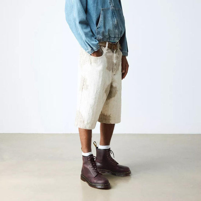 A person stands indoors against a plain background, wearing a blue denim jacket, light-colored stained knee-length shorts, white socks, and Dr Martens 1460 Cherry Red Crazy Horse Waxy Leather 8 Eye Boots., 190665786835, 190665786842, 190665786859, 190665786873, 190665786880, 190665786897, 190665786910, 50000, 50001, 50002