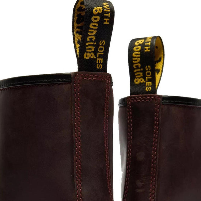 Close-up of two Dr Martens 1460 Cherry Red Crazy Horse Waxy Leather 8 Eye Boots with yellow and black pull tabs reading WITH BOUNCING SOLES in uppercase., 190665786835, 190665786842, 190665786859, 190665786873, 190665786880, 190665786897, 190665786910, 50000, 50001, 50002